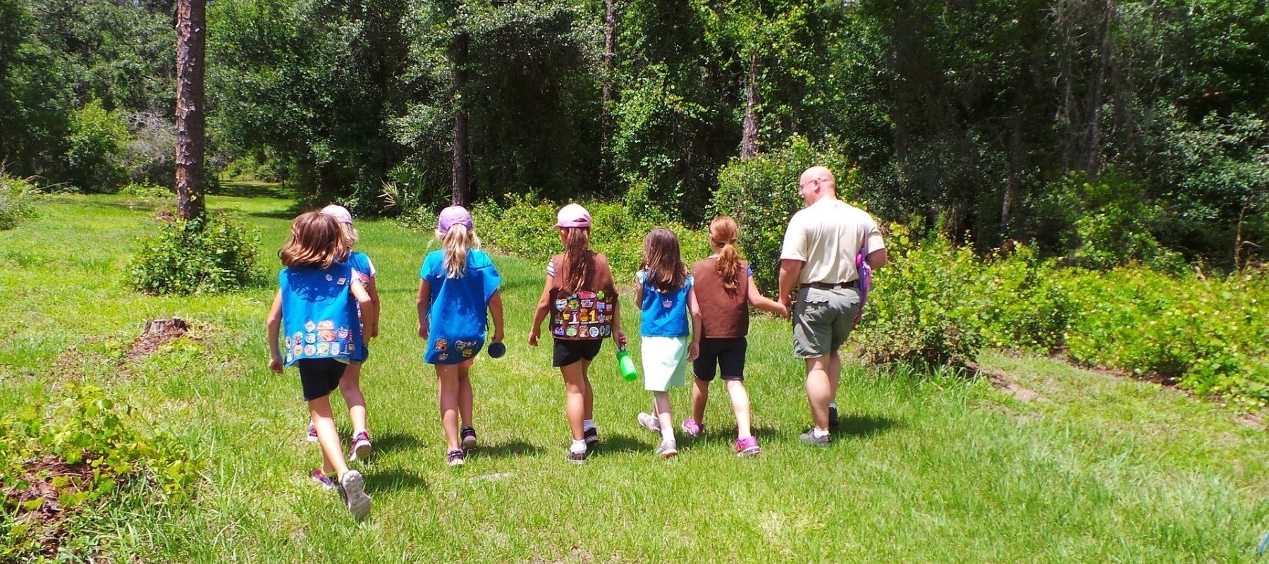 Girl scout club walking through forest with leader